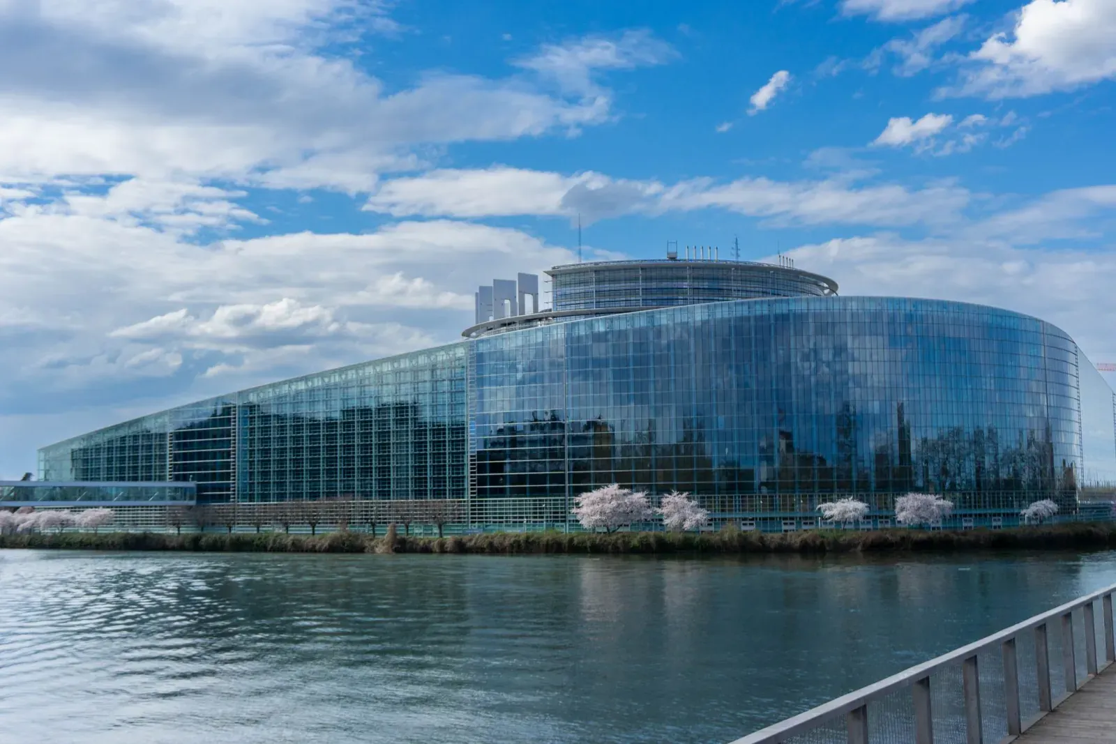 The glass facade of the European Parliament building in Strasbourg, seen across the river under a blue sky