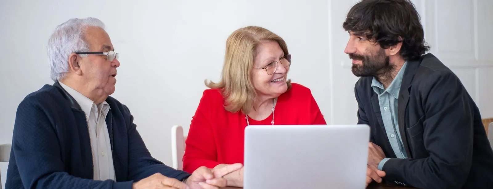 Een adviseur loopt met een ouder echtpaar hun opties door aan een tafel met een laptop, en alle drie glimlachen